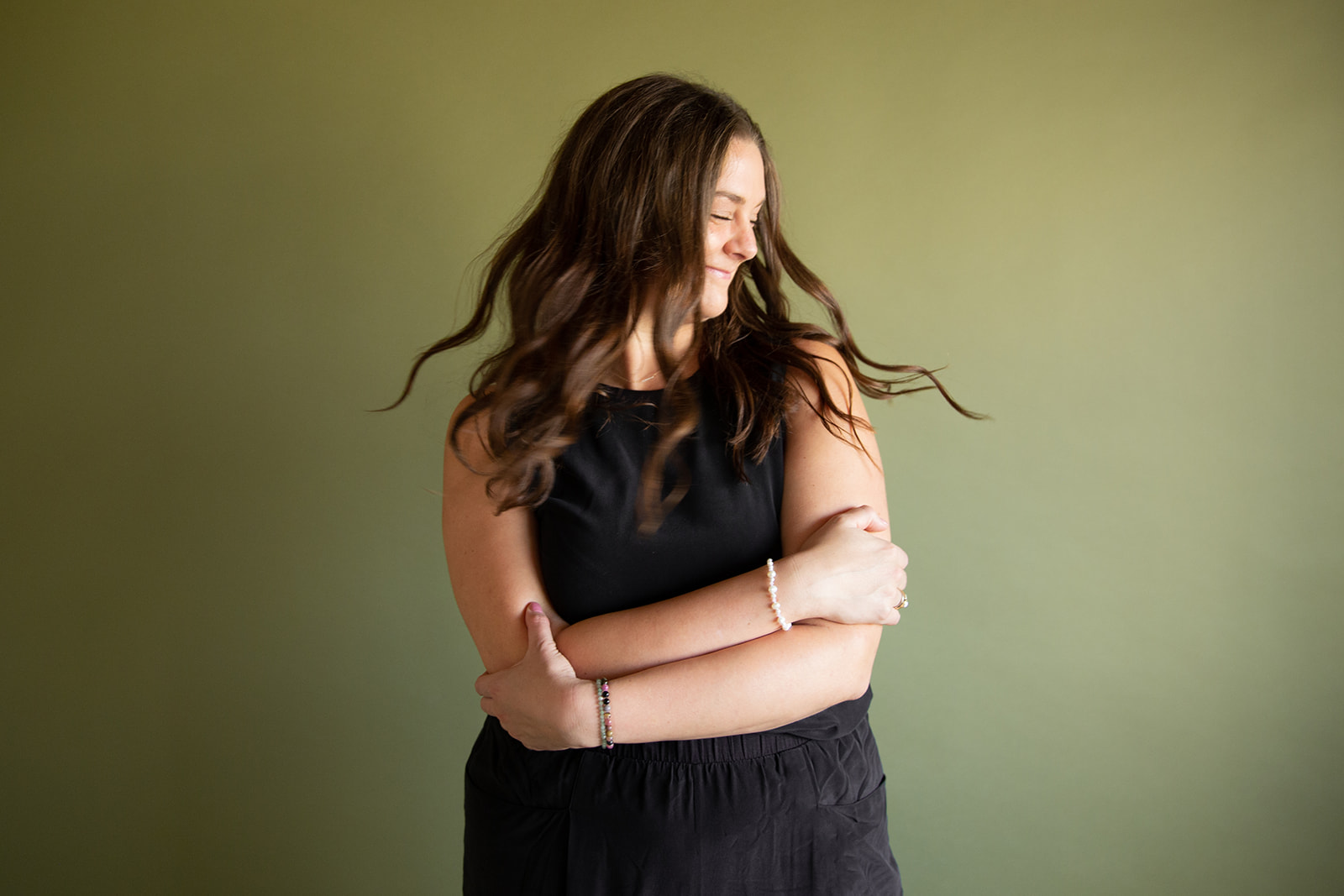 Heather Flynn in a black dress against an olive studio backdrop, arms crossed in a calm, confident pose